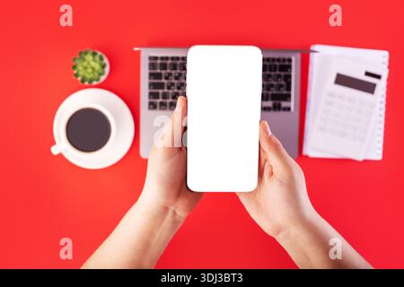 Top view photo of white calculator and notebook, grey laptop on isolated red background with holding hands smartphone. mockup Stock Photo