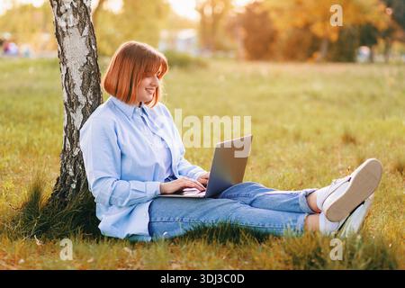 Photo portrait of pretty young woman smiling teeth sitting in green park working on laptop smiling Stock Photo