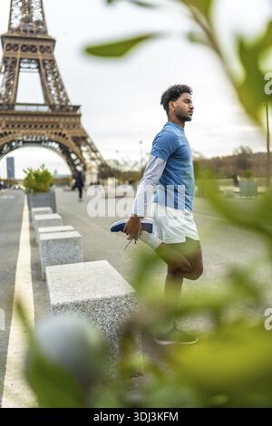 Young athletic man in sportswear stretching his quadriceps on a paris street with the eiffel tower in the background, preparing for a run and showcasi Stock Photo