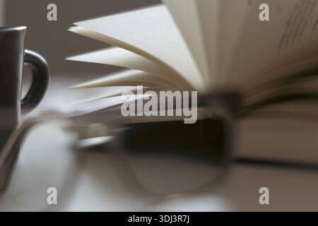 Close-up of an open book, blurred glasses and cup in the background, symbolic image for literature and reading, Cologne, North Rhine-Westphalia, Germa Stock Photo