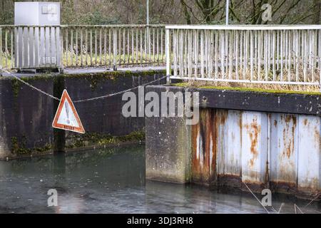 Warning sign hanging on a chain across a canal lock with rusty floodgate and concrete walls Stock Photo