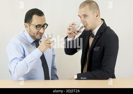 Two entrepreneur men in business attire enjoy a whiskey drink together, suggesting a casual break, alcoholic beverage, prost, cheers, drinking habit, Stock Photo