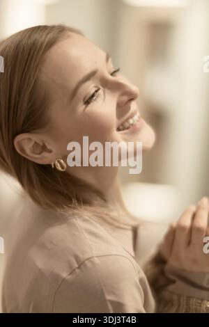 Close-up of a smiling woman in a beige outfit, looking content and happy, ease, carefree, elated, elegance, happiness, joyful, jovial, bliss, convivia Stock Photo