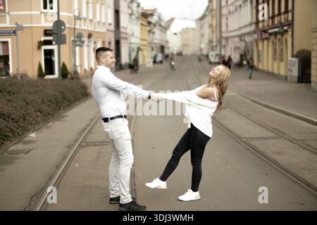 A couple playfully holding hands while balancing on tram tracks in a city setting, playfulness, playful, romance, partnership, couple, date, ease, eas Stock Photo
