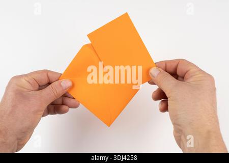 an open orange envelope in the hands on a white surface Stock Photo