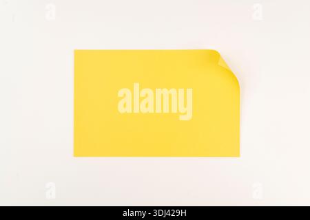 a blank yellow sheet of paper with a curled corner on a white surface Stock Photo