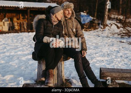 Happy couple sitting on log in snow Stock Photo