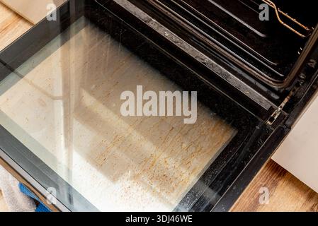 Oven with an open dirty door smeared with old dried grease, kitchen appliances equipment Stock Photo