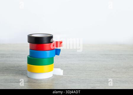Stack of colorful electrical tape rolls on a wooden surface with white background Stock Photo