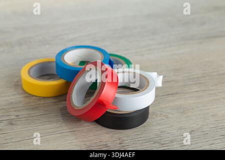 Six rolls of colored tape yellow, blue, green, red, white, black close up on wood. Stock Photo
