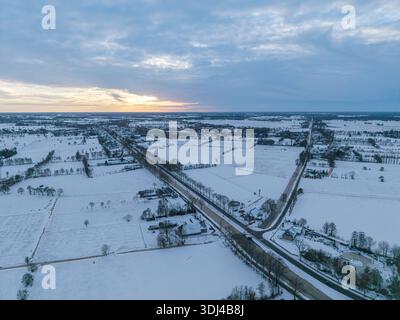 Aerial sunset over the snow-covered Dutch landscape, with glowing golden clouds and white fields. Stock Photo