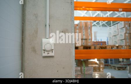 Thermostat mounted on concrete wall inside modern warehouse, HVAC and energy control concept in industrial building. Stock Photo