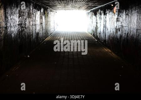 Dark underground pedestrian tunnel with bright light at the end, strong contrast and symmetry. Graffiti walls, empty passageway, urban concept of hope Stock Photo