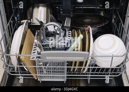Open dishwasher filled with clean dishes and kitchen utensils. Modern household appliance after washing cycle. Everyday home routine concept focused. Stock Photo