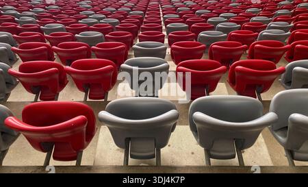 Rows of empty red and grey plastic seats inside a large modern stadium with no spectators. Stock Photo