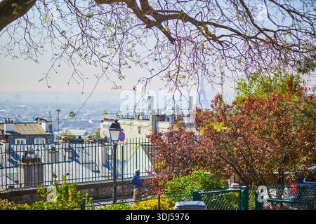 Scenic view of the Eiffel Tower in the distance, seen through budding spring branches and colorful foliage on Montmartre hill in Paris, France. Stock Photo