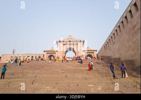Varanasi, India - March 19, 2024: People are seen walking, sitting, and gathering on the large stone staircase leading to the entrance archway of Vishalakshi Temple, with security personnel and handrails visible during daylight. Stock Photo