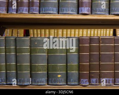 Vintage leather-bound books with gold lettering arranged on wooden library bookshelves Stock Photo