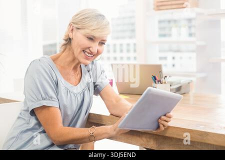 Tablet and open laptop are resting on wooden desk near large windows with colored pens. Office, cityscape, daylight, modern, professional, productivit Stock Photo