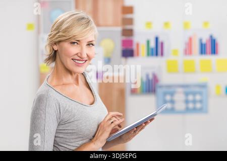 Woman is smiling and interacting with tablet in office planning area with charts and sticky notes. Professional, collaboration, graphs, diagrams, work Stock Photo