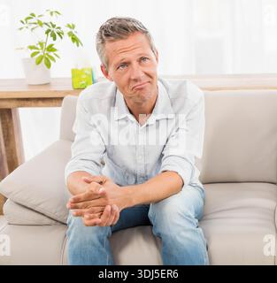 Beige leather sofa sitting in bright living room with sheer curtains diffusing natural light. Couch, interior, home, wooden, plant, console, minimal Stock Photo