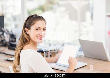 Tablet is displaying blank white screen beside open laptop on wooden desk near bright window. Woman, workspace, focus, coworking, modern, minimal, nat Stock Photo