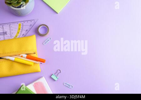 School supplies, notepad, yellow pencil-case, pencil, ruler, succulent plant and paper clips on purple background. Top view, flat lay, copy space. Stock Photo