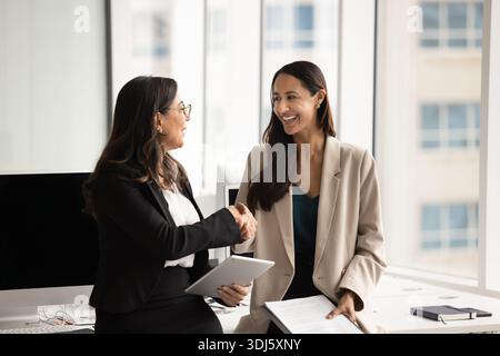 Two happy professional women shaking hands, finalizing meeting Stock Photo