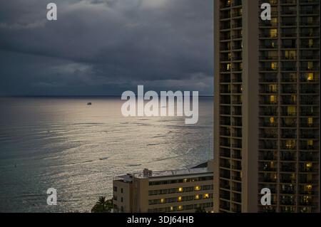 Dramatic evening seascape of Waikiki beach with hotel balconies in foreground and boats on horizon. Stock Photo