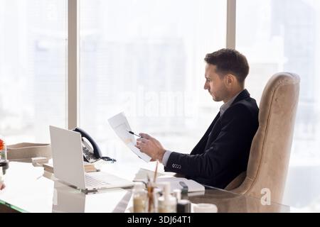 Serious Latin businessman checking paper sales report at workplace Stock Photo