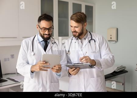 Friendly experienced healthcare specialist consulting younger colleague using digital tablet Stock Photo