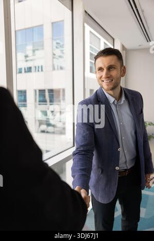 Businessman in jacket shaking hands colleague standing un modern office Stock Photo