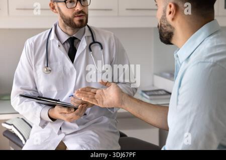 Closeup focused male doctor holding clipboard pen listening to patient Stock Photo