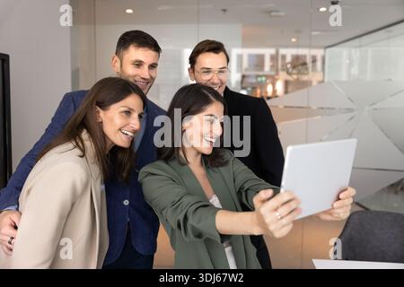 Four colleagues gather to take group selfie on digital tablet Stock Photo