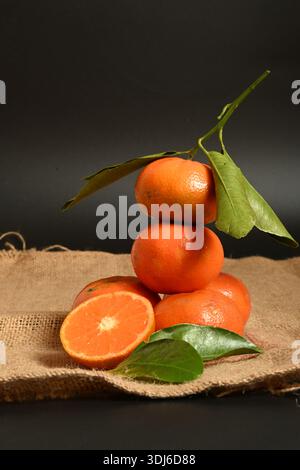 High-quality vertical shot of fresh mandarins with leaves on rustic burlap, ideal for organic food labels and juice packaging Stock Photo