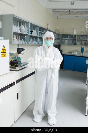 Clinical lab is showing full white protective suit centered, microscope and biohazard cabinet. Sterile, cleanroom, hazmat, researcher, laboratory, flu Stock Photo