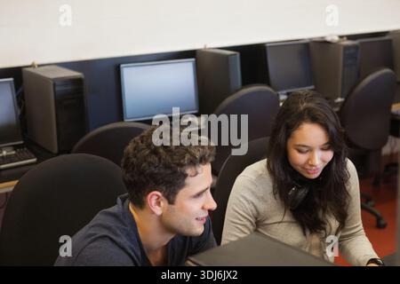 Diverse classmates collaborating on PCs in computer lab, headphones and keyboards shown. Students, peers, classroom, monitors, teamwork, focus, educat Stock Photo