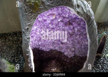 A large geode with a purple amethyst crystal interior, partially embedded in a rock formation Stock Photo