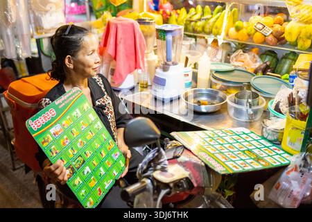 Siem Reap Province,Cambodia-April 02 2025: At a streetfood stall,next to the Siem Reap River in the city center,the woman cooking food tempts passers- Stock Photo