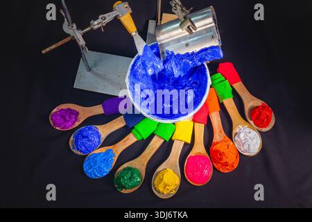A creative arrangement of colorful paint on wooden spoons surrounding a central bucket of orange paint with spatulas, symbolizing artistic expression, Stock Photo