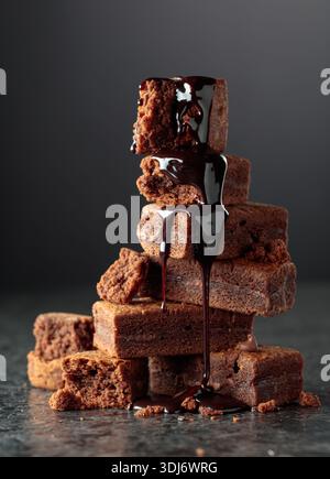 Brownie pieces on a black background. Melted chocolate drips down the brownie. Stock Photo
