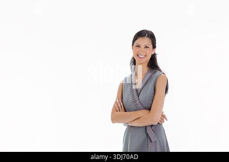 Asian woman standing, smiling, facing camera in studio wearing gray wrap dress sash, copy space. Portrait, professional, corporate, minimal, clean, ne Stock Photo