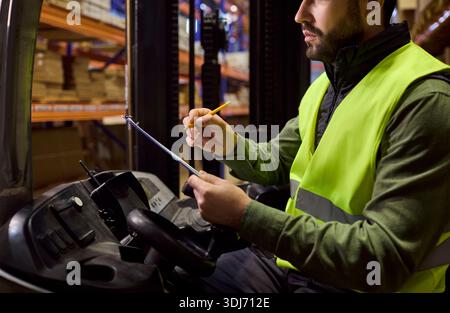 Forklift operator checking clipboard for inventory in warehouse loading goods Stock Photo