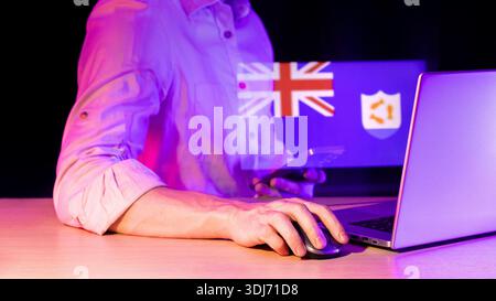 Hand on mouse adjacent to laptop keyboard, purple tinted dark backdrop, holographic overlay of union flag pattern and circular shield icon. Stock Photo