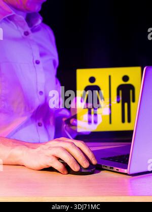 Hand on mouse, laptop displaying yellow signs for both female and male genders in violet lighting. Stock Photo