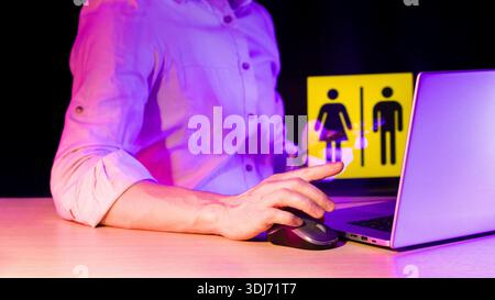Arm using computer mouse, display featuring yellow dual gender signs in dramatic purple lighting. Stock Photo
