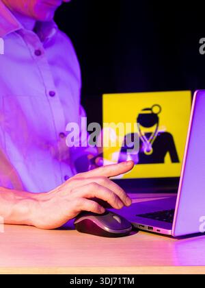 Man's hand gesturing towards laptop, semi-transparent yellow icon of masked female with stethoscope in purple glow. Stock Photo