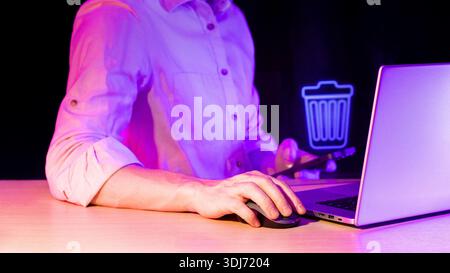 Close-up of index finger contacting blue neon holographic delete symbol beside laptop in purple ambiance. Stock Photo