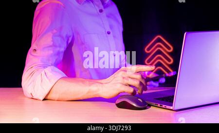 Close view of interactive tech session with pointing hand, laptop, and glowing upload arrows hologram over gadget in low light Stock Photo