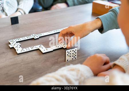Hands placing domino tiles on a wooden table, enjoying leisure time Stock Photo